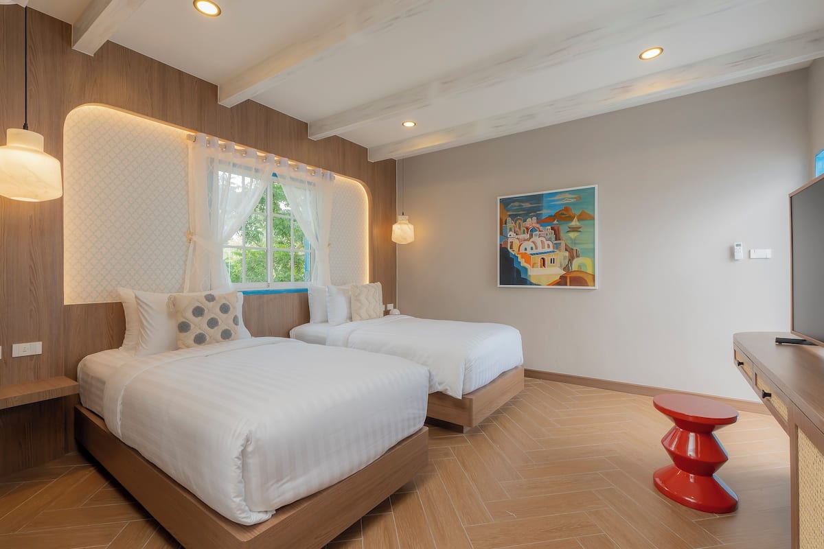 Een hotelkamer met twee bedden, een raam met uitzicht, een schilderij aan de muur en een rode tafel.
