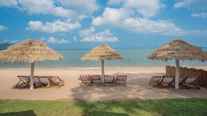 Una playa con tres sombrillas de paja y sillas de descanso.