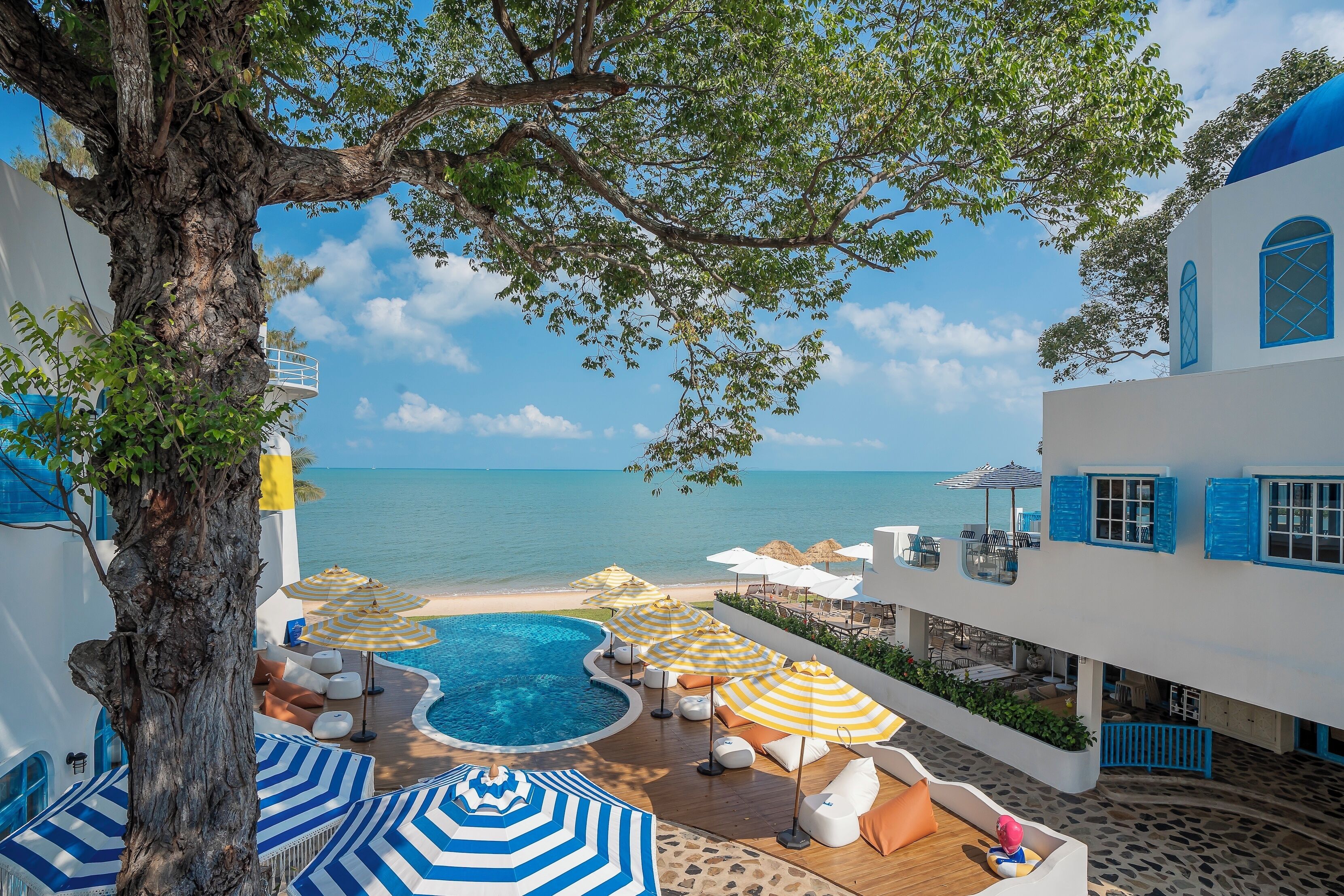Área da piscina com espreguiçadeiras e guarda-sóis, com vista para uma praia e o mar.