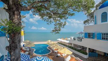 Área da piscina com espreguiçadeiras e guarda-sóis, com vista para uma praia e o mar.