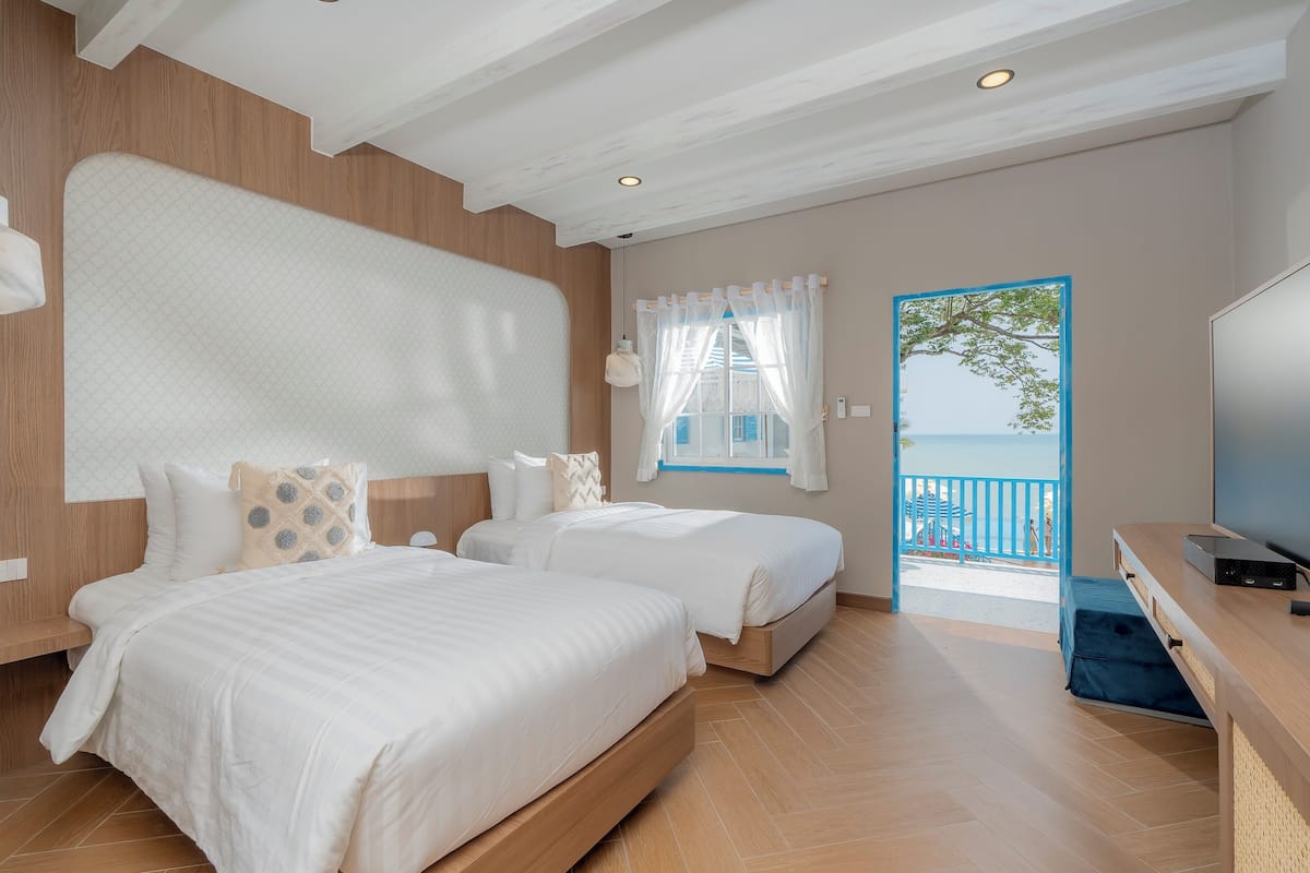 Een slaapkamer met twee bedden, een televisie en een balkon met uitzicht op zee.