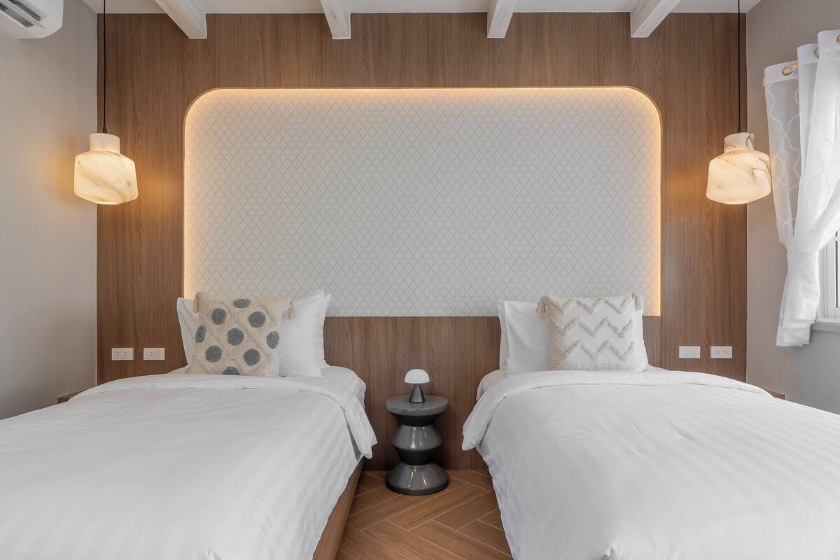 Een moderne slaapkamer met twee bedden, een houten hoofdbord en een klein nachtkastje.