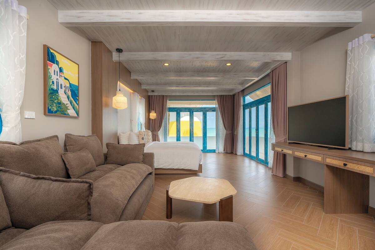 Een moderne hotelkamer met een groot bed, een bank, een televisie en uitzicht op zee.