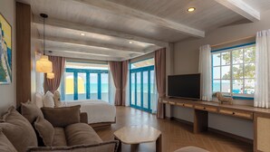 Una habitación de hotel moderna con una cama grande, un sofá, un televisor y vista al mar a través de amplios ventanales.