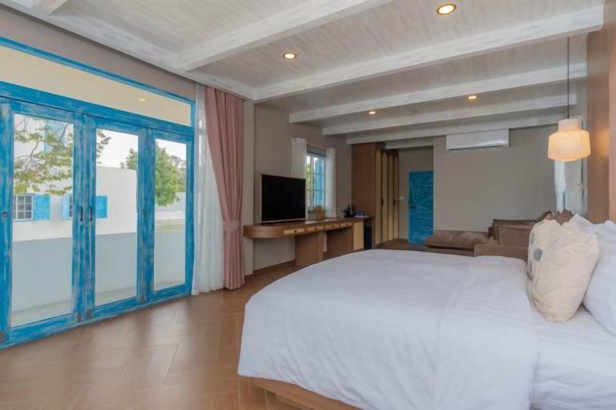 A bedroom with a large bed, a TV, and a desk. There is a sliding glass door leading to an outdoor area.
