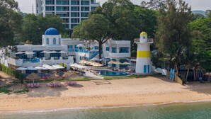 Un hotel frente a la playa con piscina, sombrillas y un faro.