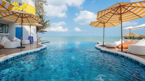 Un área junto a la piscina con sillones de descanso y sombrillas, una piscina azul cristalina y vistas al océano.