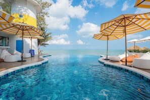 Un espace aménagé au bord de la piscine, avec des chaises longues et des parasols, une piscine à l’eau d’un bleu limpide et une vue sur l’océan.