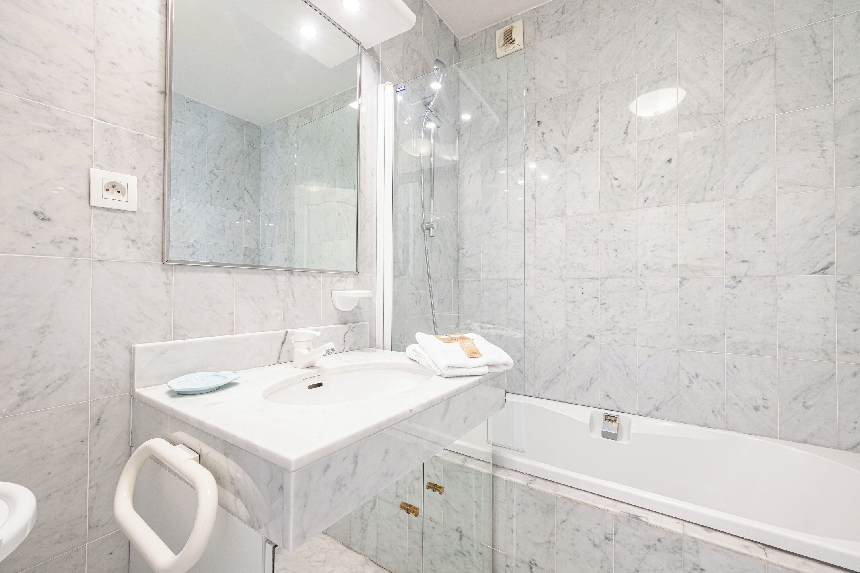 A modern bathroom with a marble sink, a glass shower enclosure, and a white bathtub.