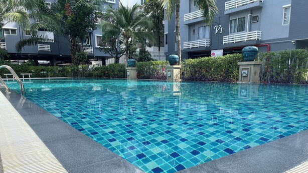 Una piscina con azulejos azules, rodeada por un deck gris y palmeras.