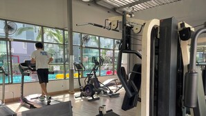 Un gimnasio con equipo de ejercicio, ventanas amplias y vistas a palmeras.