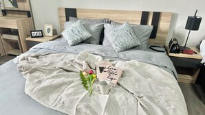 Una cama bien hecha con una manta de color claro, almohadas, un cuadro enmarco, un reloj pequeño y un libro titulado 'Love Style Life'.