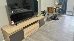 Una sala de estar moderna con un televisor de pantalla plana grande sobre un mueble bajo, un sofá, una mesa de comedor con sillas y una planta en maceta.