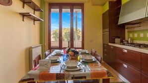 A dining area with a table set for four, a clock on the wall, and a view through the door.