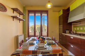 A dining area with a table set for four, a clock on the wall, and a view through the door.