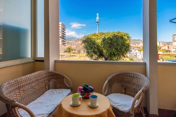 A balcony with wicker chairs, a small round table, and a bowl of fruit.