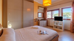 A hotel room with a bed, a TV on a stand, a dresser, and a window with curtains.