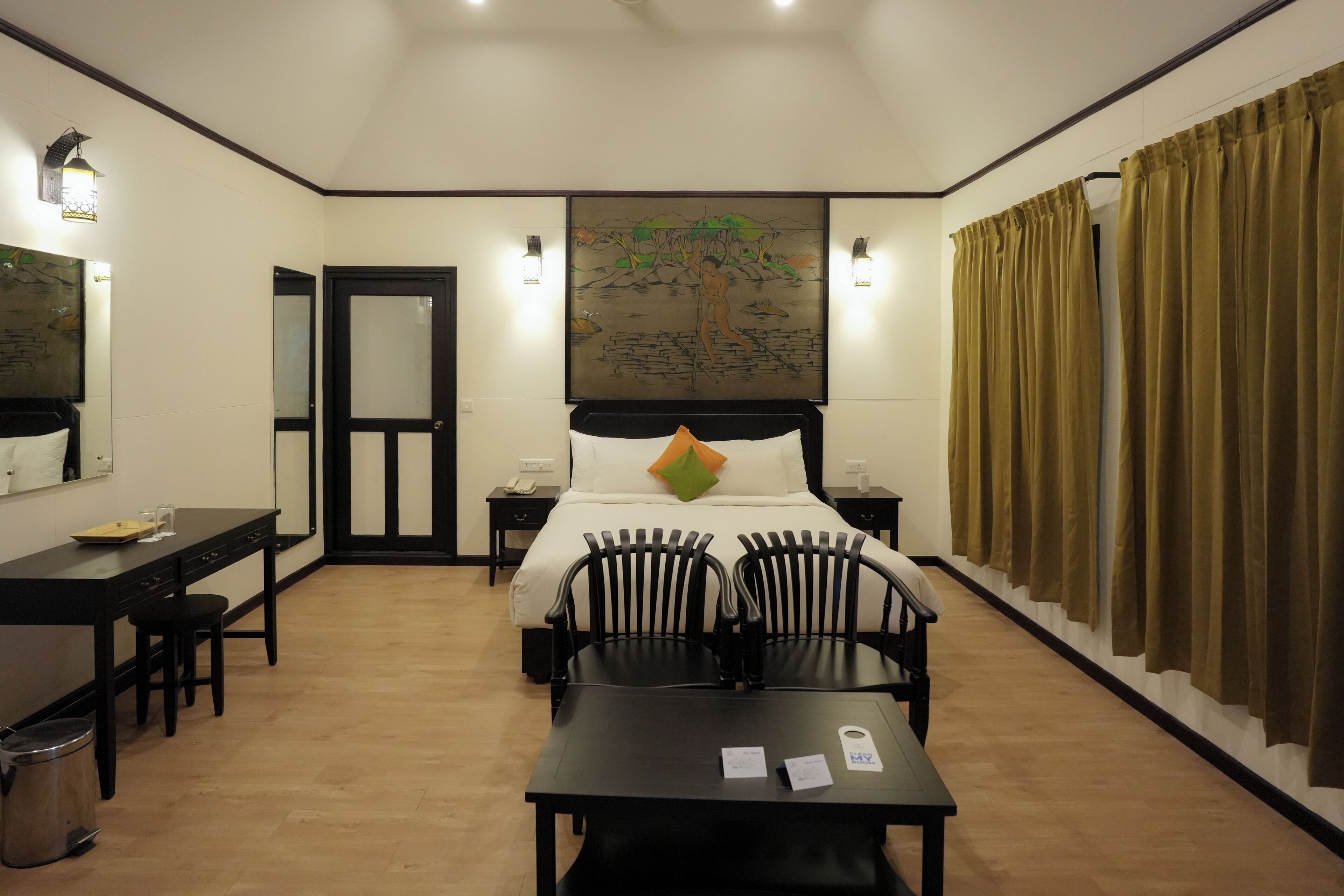 A hotel room with a bed, two bedside tables, a desk with chairs, a trash bin, and a painting on the wall.
