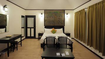 A hotel room with a bed, two bedside tables, a desk with chairs, a trash bin, and a painting on the wall.