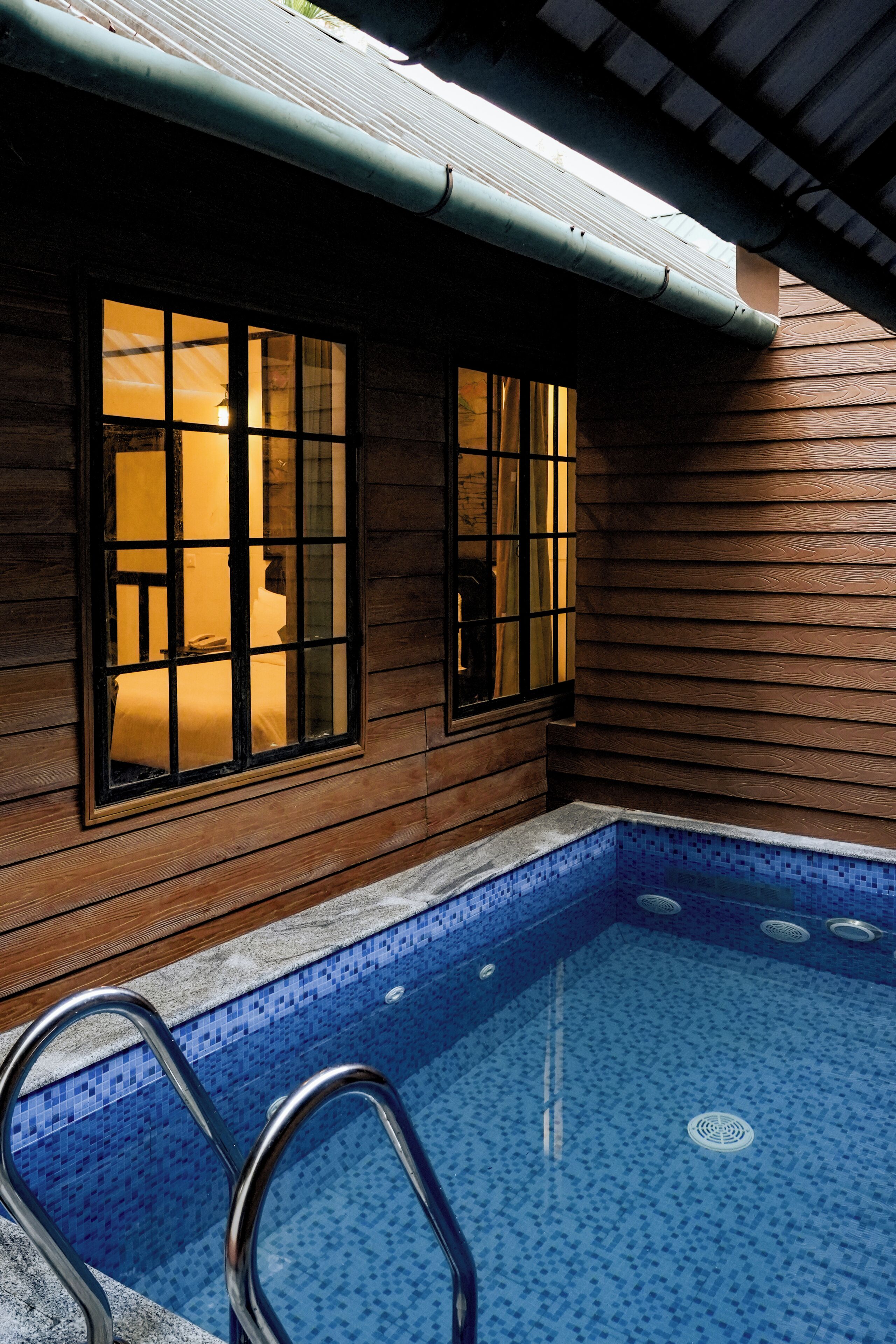A wooden cabin with a small pool and two windows.