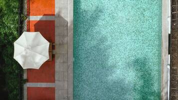 Vista aérea de una piscina rectangular con borde de azulejos, rodeada por un camino de ladrillo y césped verde.