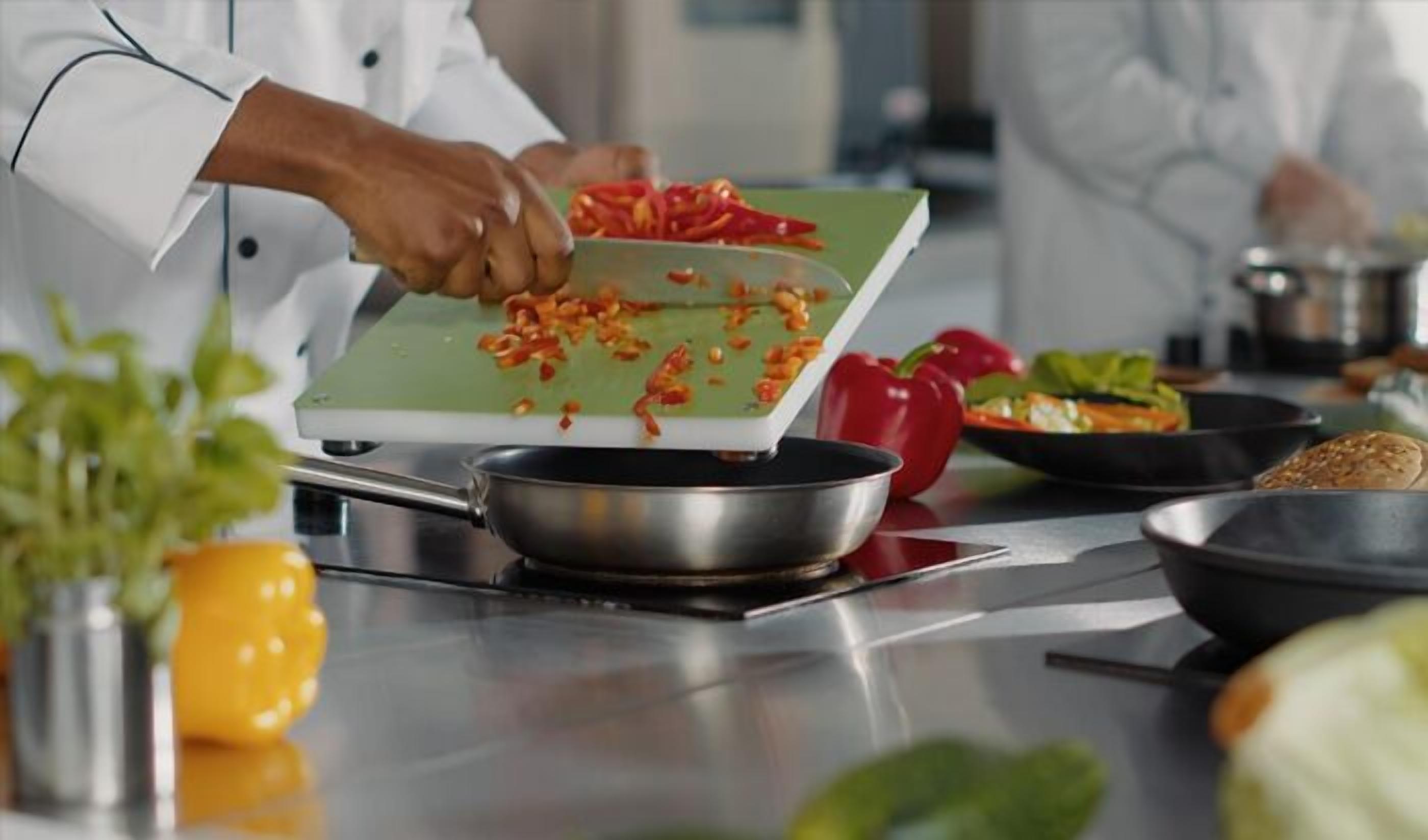 Un chef coupe des poivrons rouges sur une planche à découper.