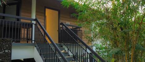 A staircase leading to a building with a balcony, surrounded by greenery.