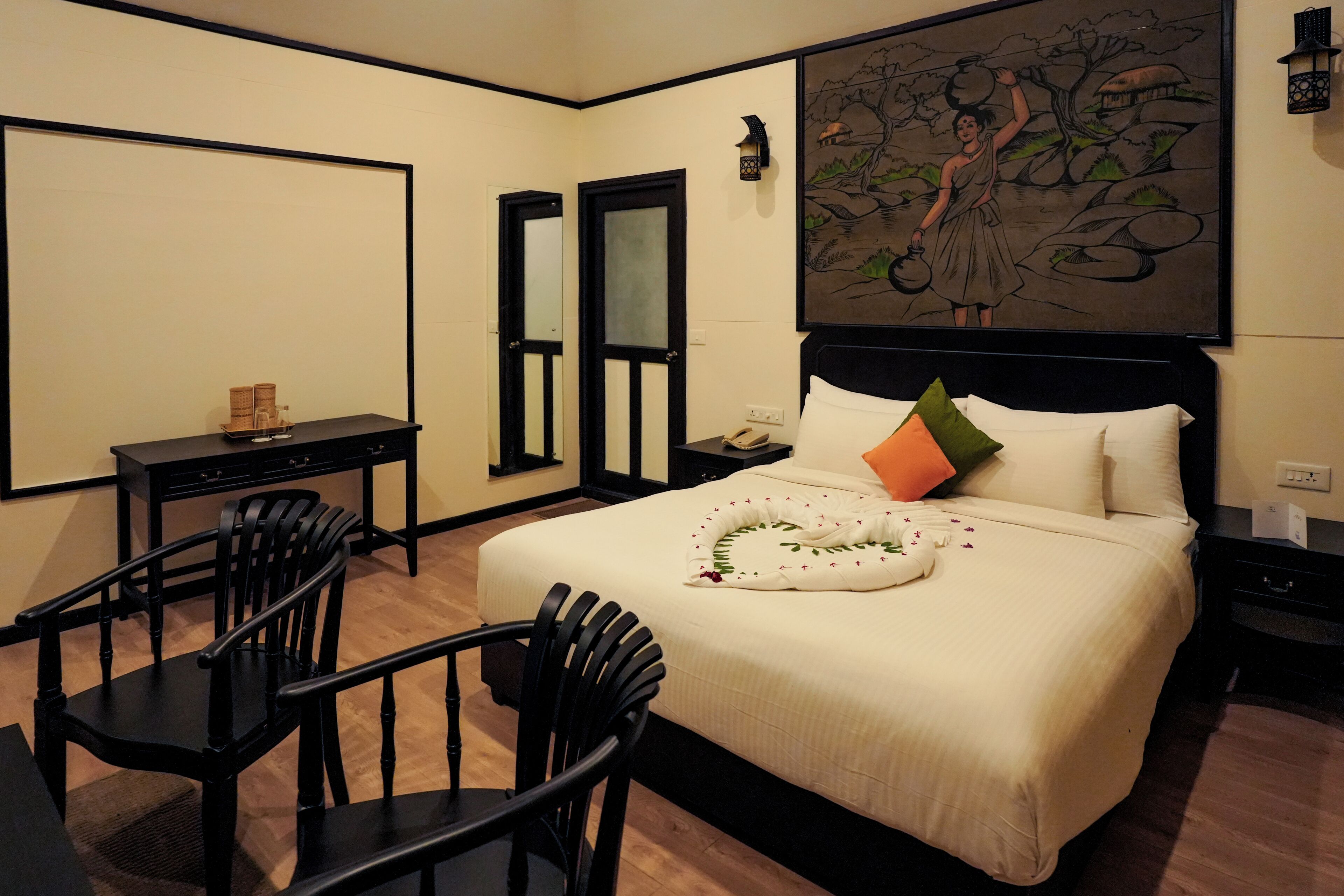 A hotel room with a large bed, a desk, two chairs, and a painting on the wall.