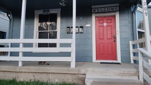 Una casa con una puerta roja, un cartel que dice 'Welcome' encima y un buzón con los números 1, 2, 3 y 4.