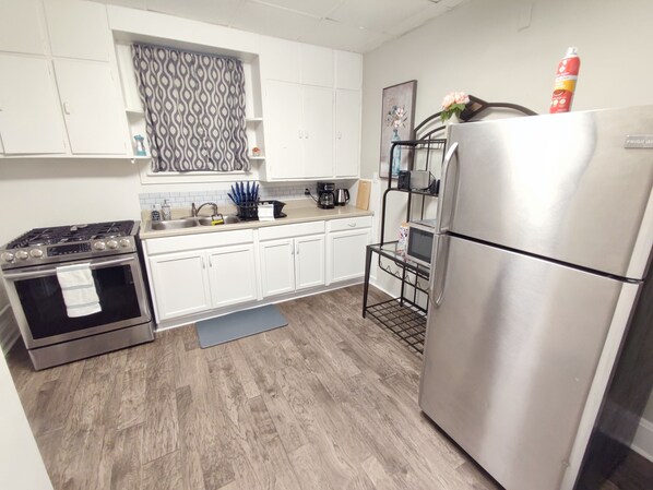 Una cocina moderna con armarios blancos, un refrigerador de acero inoxidable, una estufa a gas y un microondas.