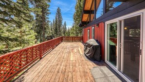 Une terrasse en bois avec une rambarde rouge, un barbecue et une porte vitrée donnant sur un espace abrité.