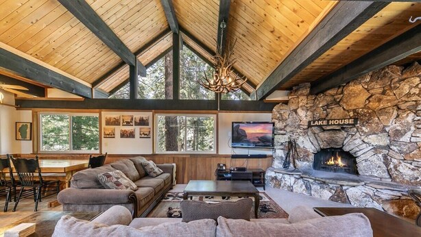 Un salon chaleureux avec une cheminée en pierre, des poutres en bois et une grande fenêtre donnant sur une forêt.
