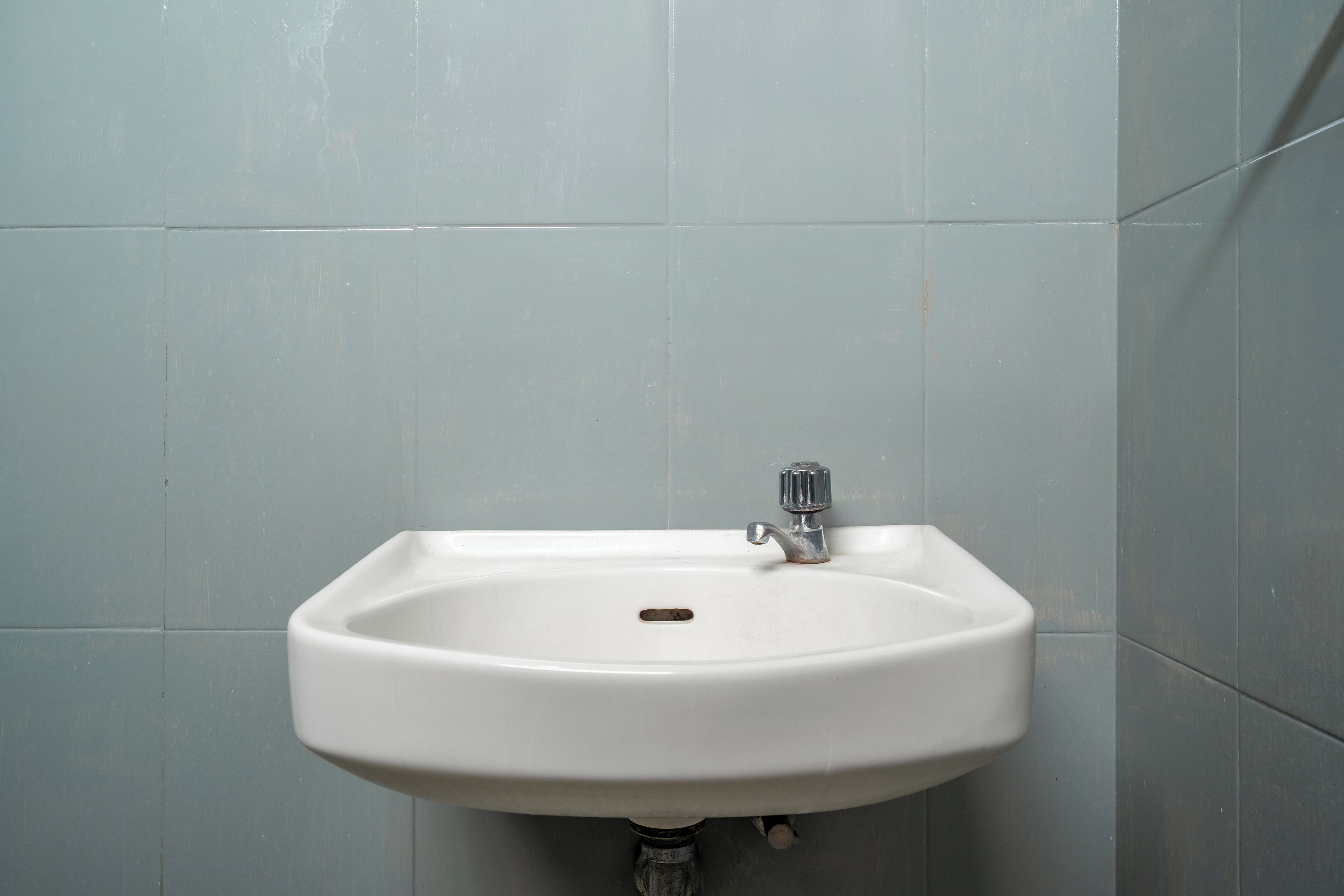 A white bathroom sink with a chrome faucet, set against a tiled wall.