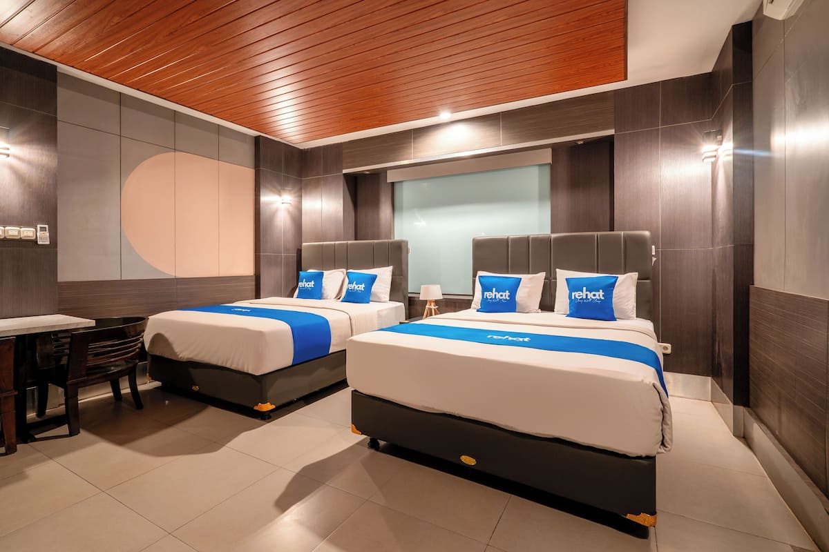 A modern hotel room with two beds, a desk, and a large window.