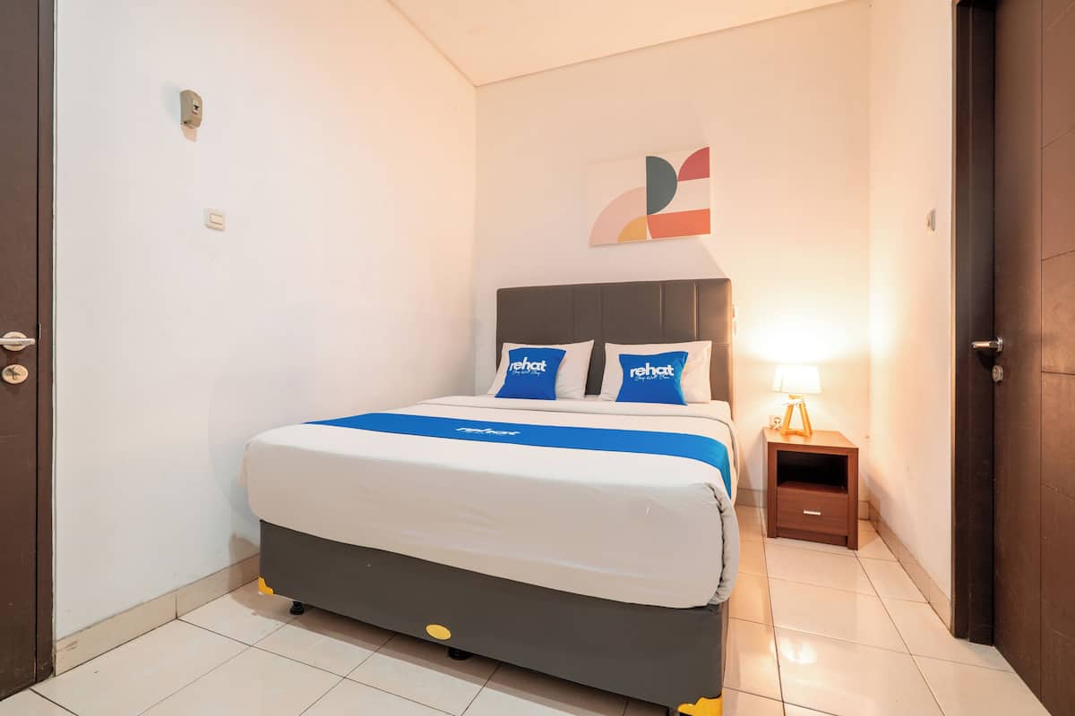 A hotel room with a bed, a nightstand, a wall clock, and a door.