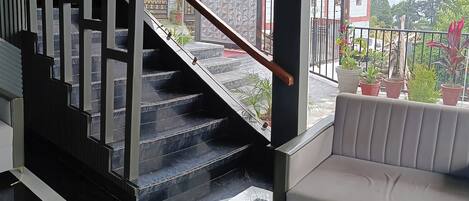 A modern interior with a staircase leading to a balcony, a white sofa, and a view of a residential area.