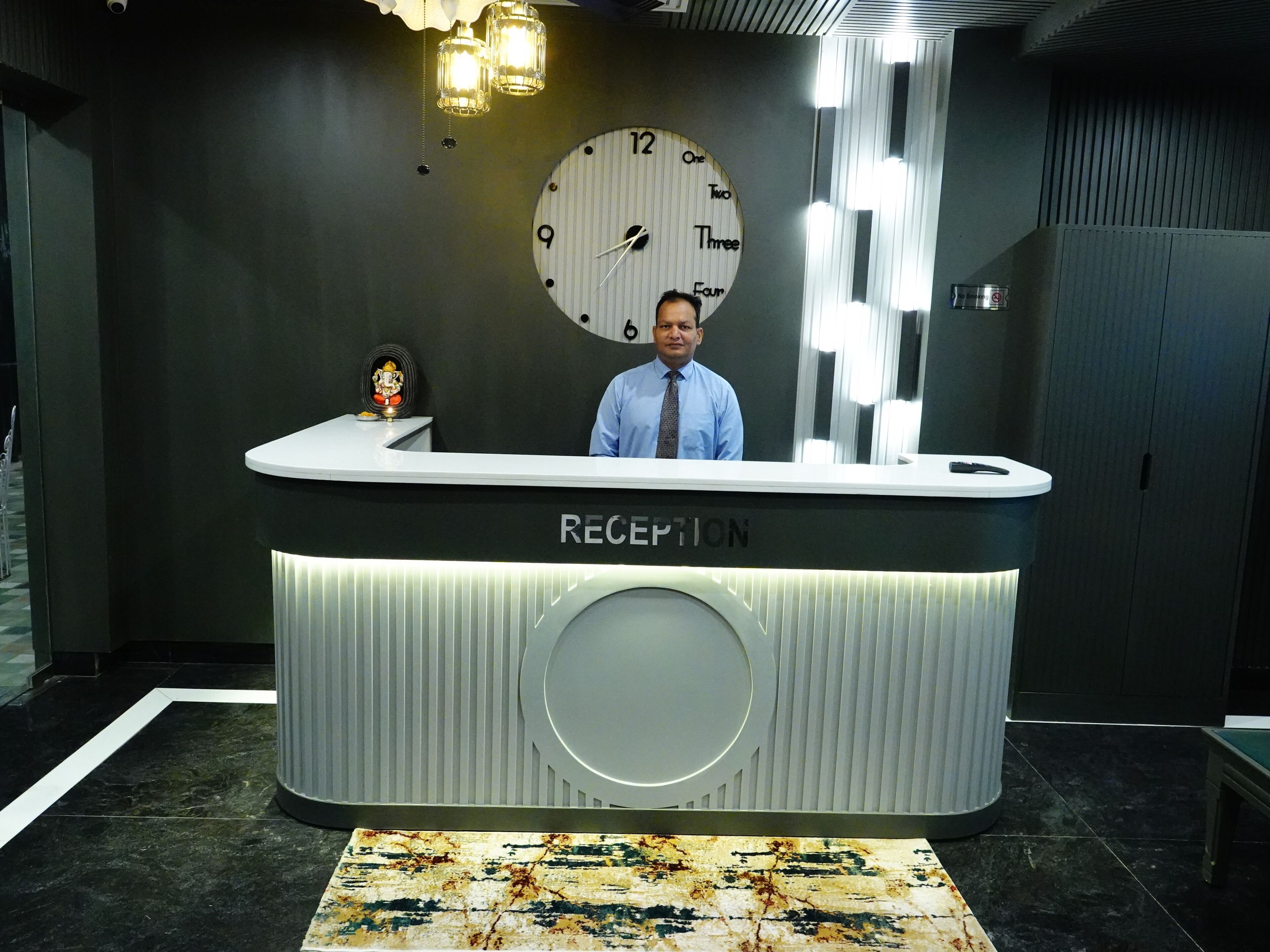 Un mostrador de recepción con un reloj, una pequeña estatua y una alfombra estampada.