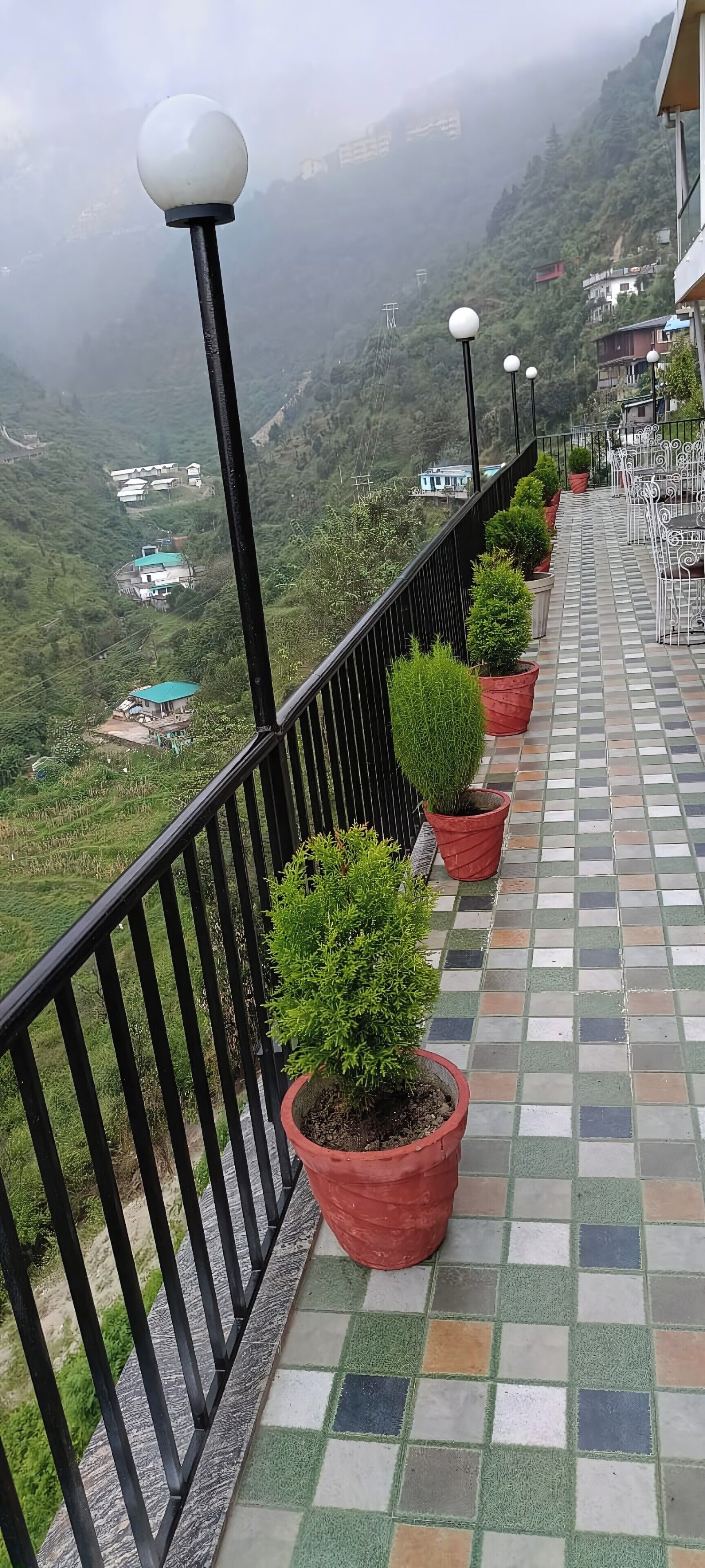 A balcony with potted plants, a tiled floor, and a view of a mountainous landscape.