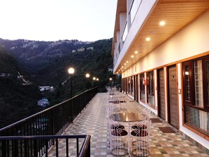A balcony with tables and chairs, overlooking a mountainous landscape. - Rubystone Mussoorie A Leisure Resort (Dehradun)