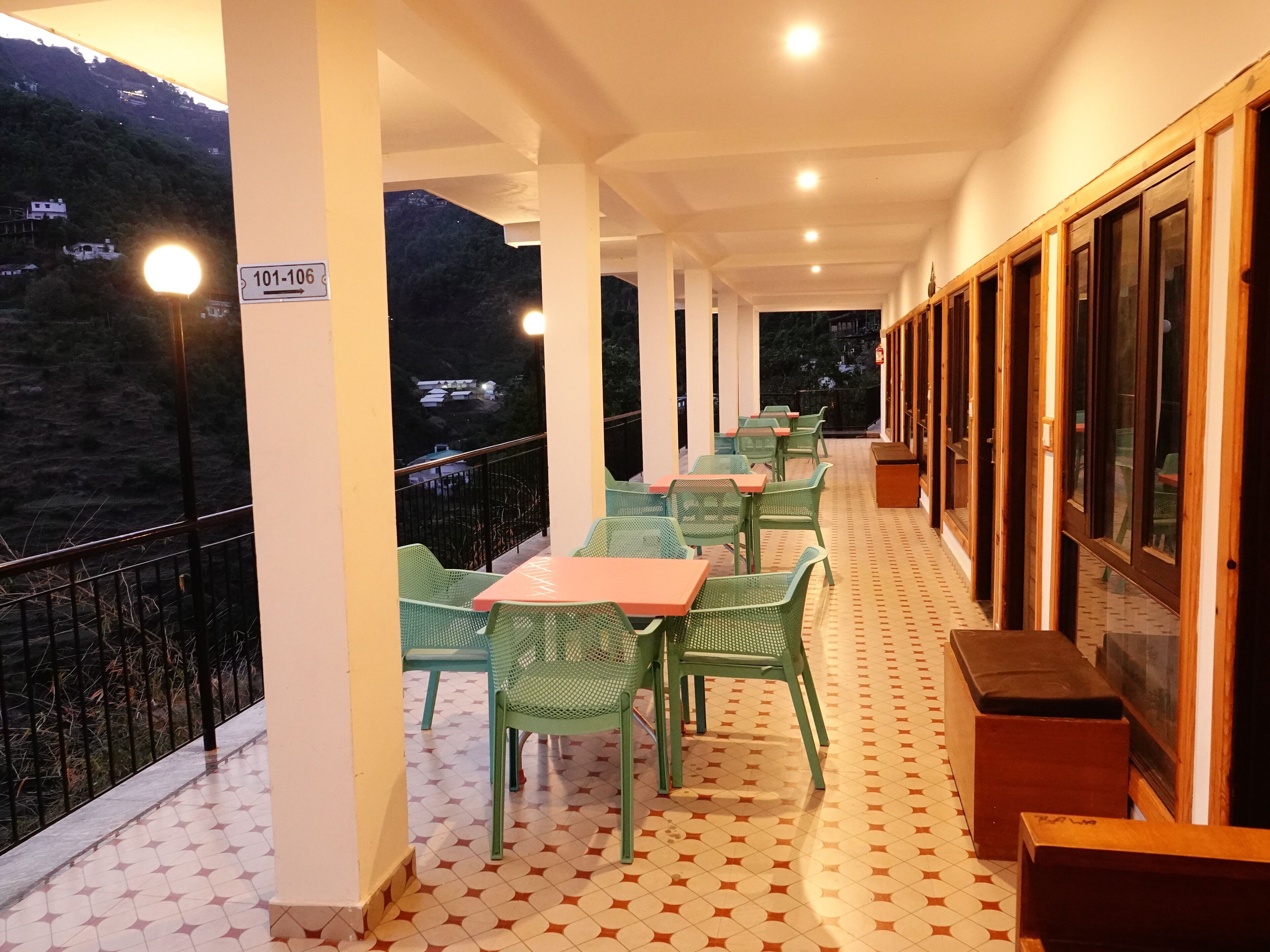 A covered outdoor seating area with tables and chairs, a patterned floor, and a view of a hillside.