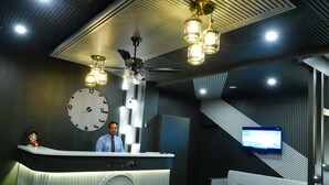 A reception area with a modern design, including a reception desk, a clock, a sofa, and a television screen. - Rubystone Mussoorie A Leisure Resort (Dehradun)