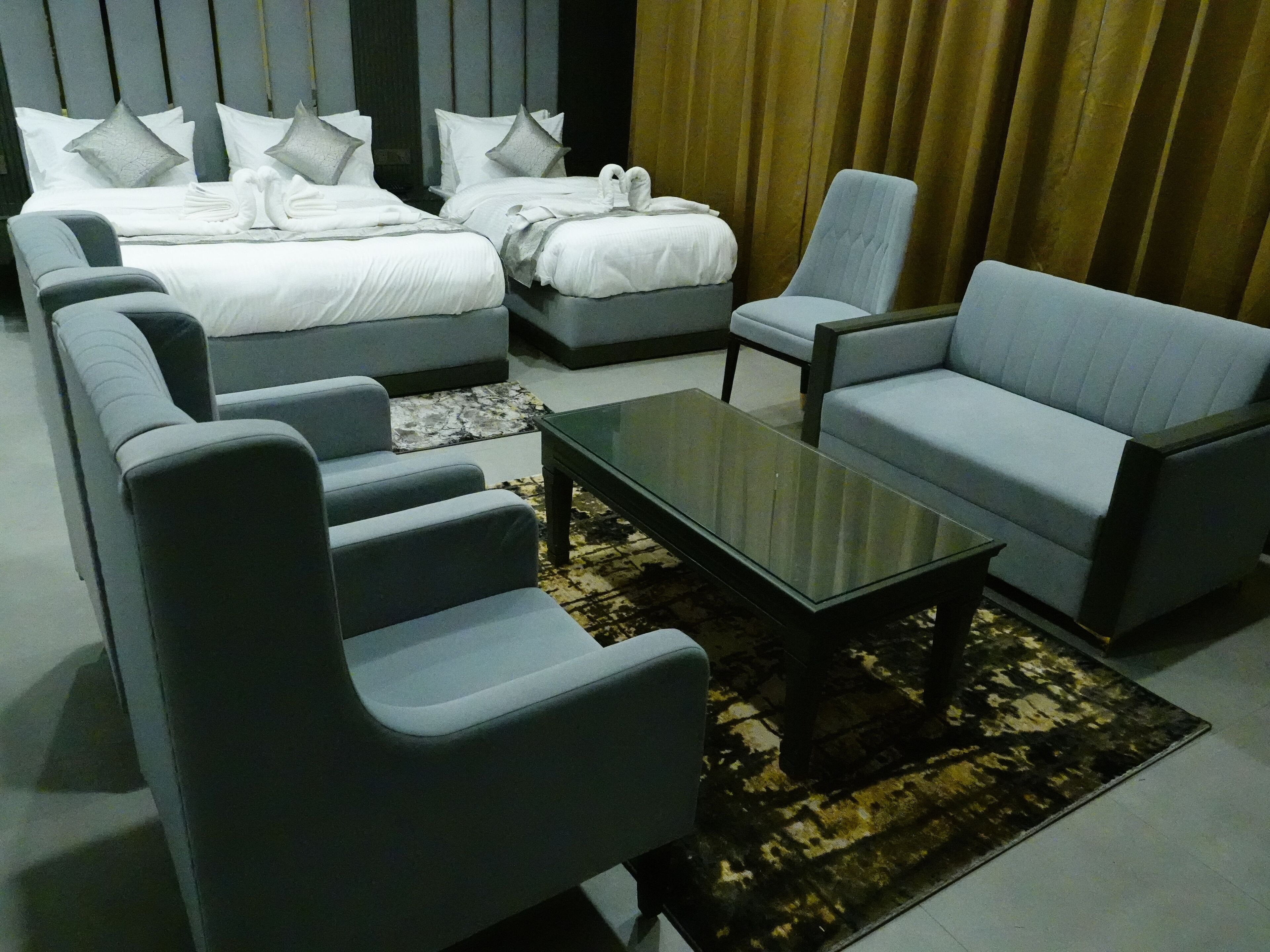 A modern hotel room with a large bed, two sofas, a coffee table, and a patterned rug.