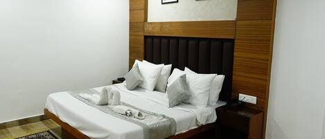 A neatly made bed with white bedding and a grey throw, a wooden headboard, and a small bedside table with a lamp.