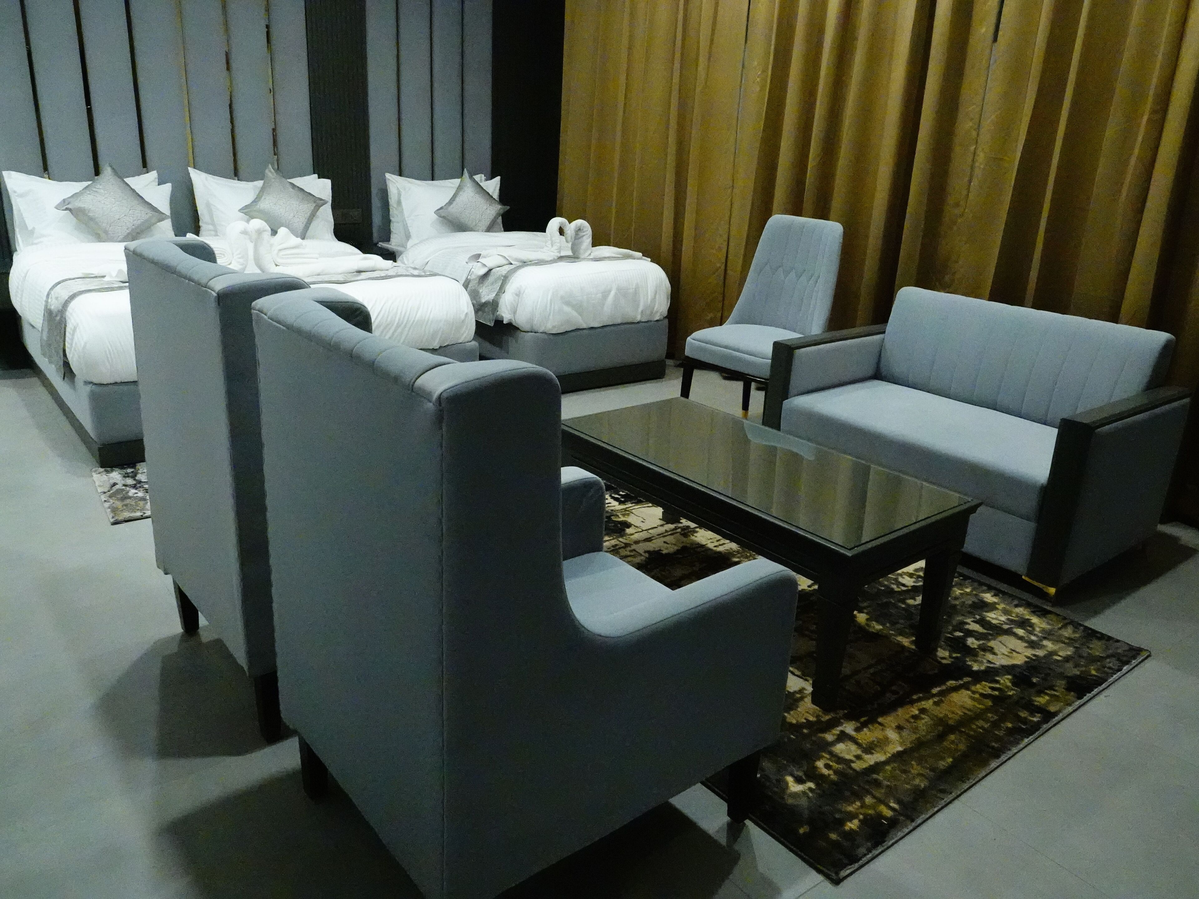 A modern hotel room with a sofa set, a small table, and a bed with white linens and grey pillows.