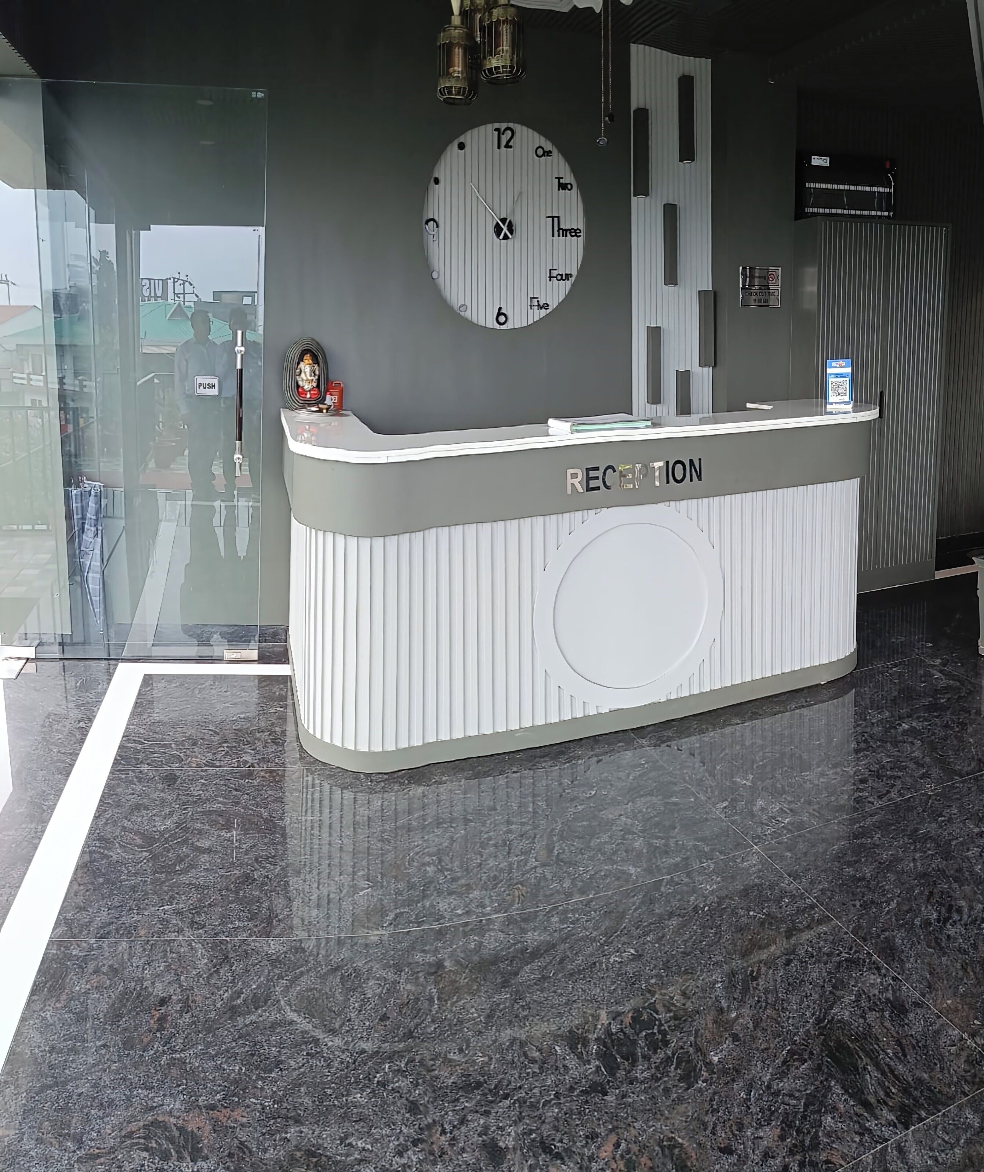 Una reception con una sveglia sopra, un pulsante a pressione e un codice QR sul bancone.