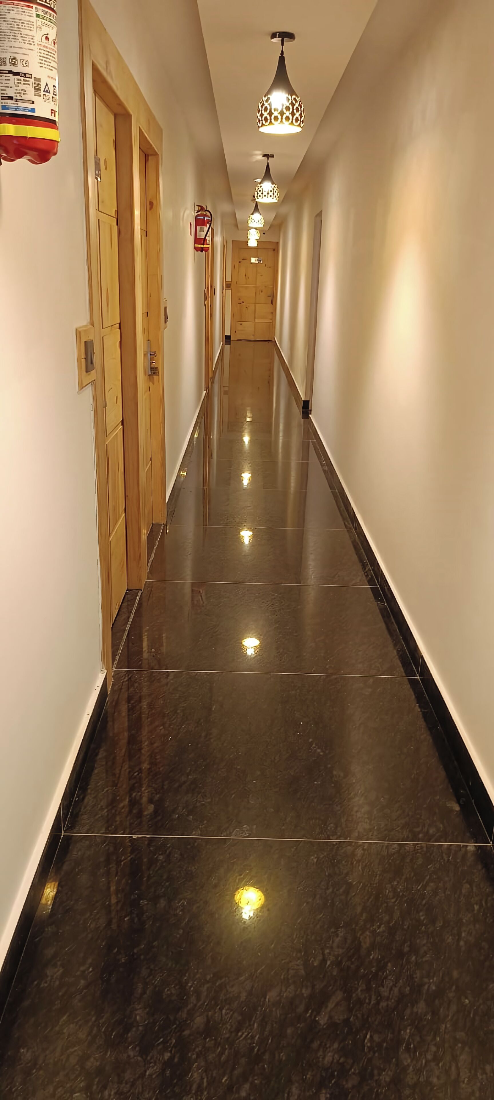 A long, narrow hallway with polished dark tiles, wooden doors, and hanging pendant lights.
