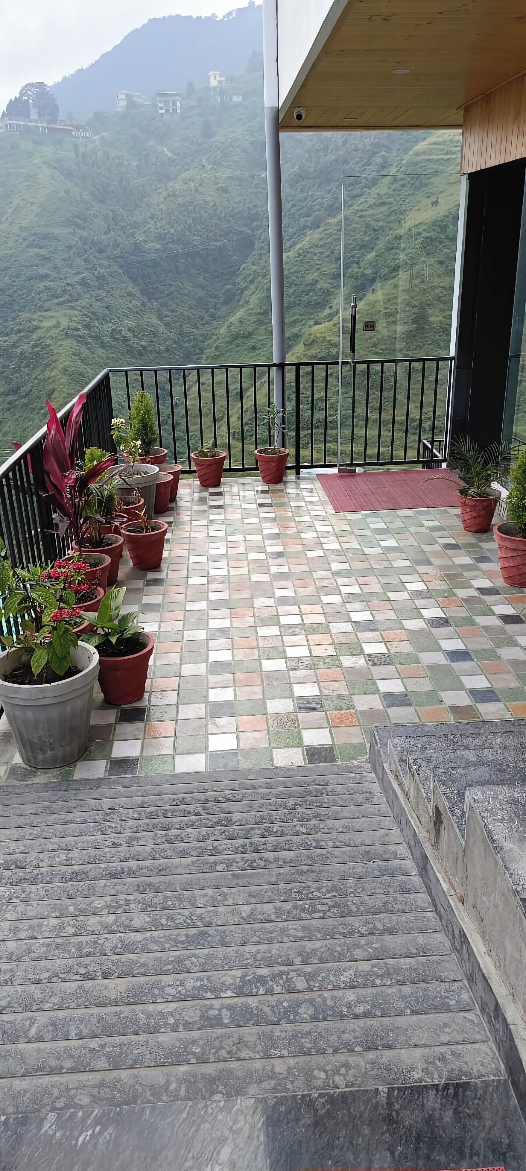 A balcony with potted plants, a tiled floor, and a view of a mountainous landscape.