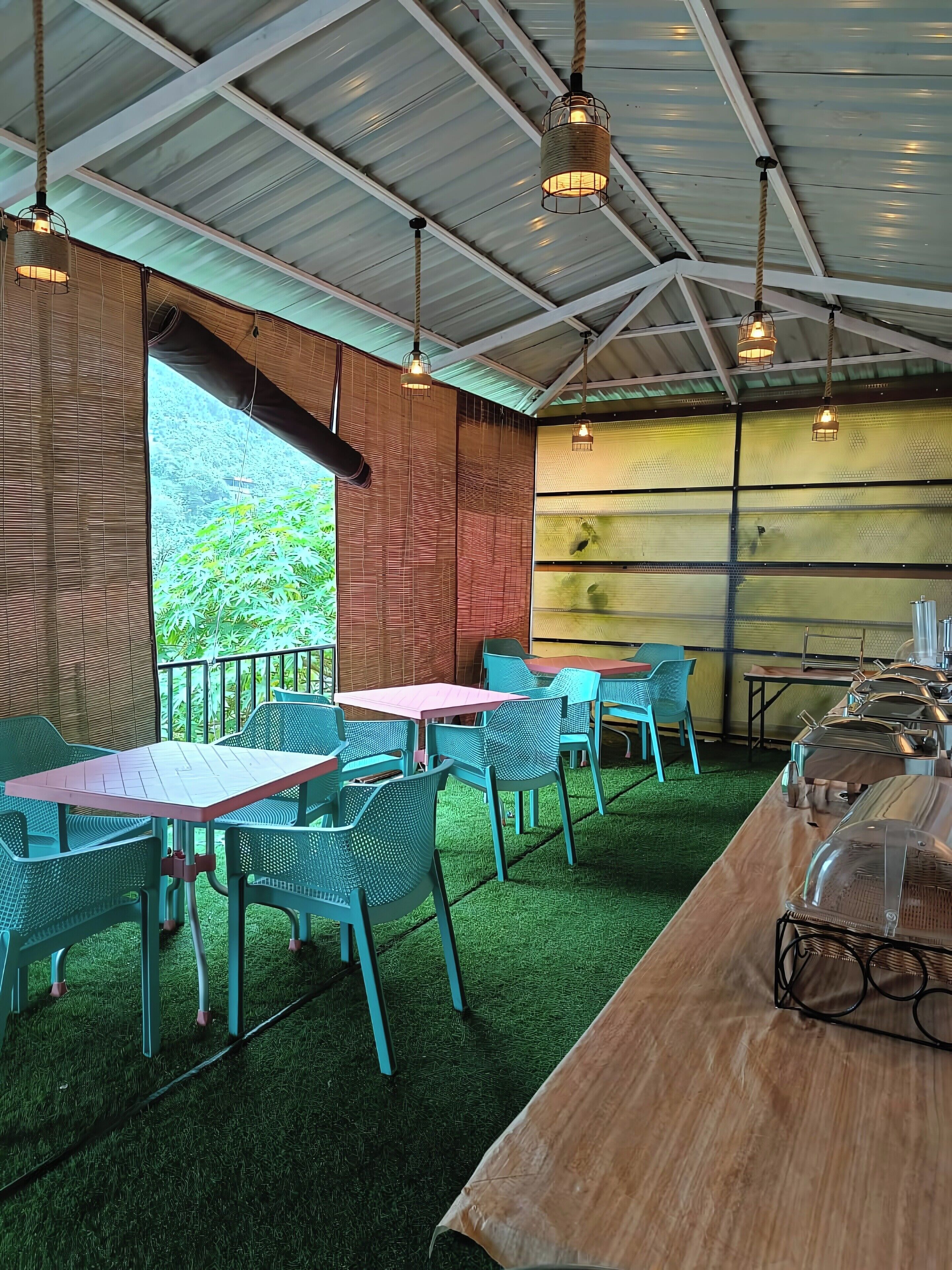 Un área de estar al aire libre con mesas y sillas, una mesa de madera con una parrilla y luces colgantes.
