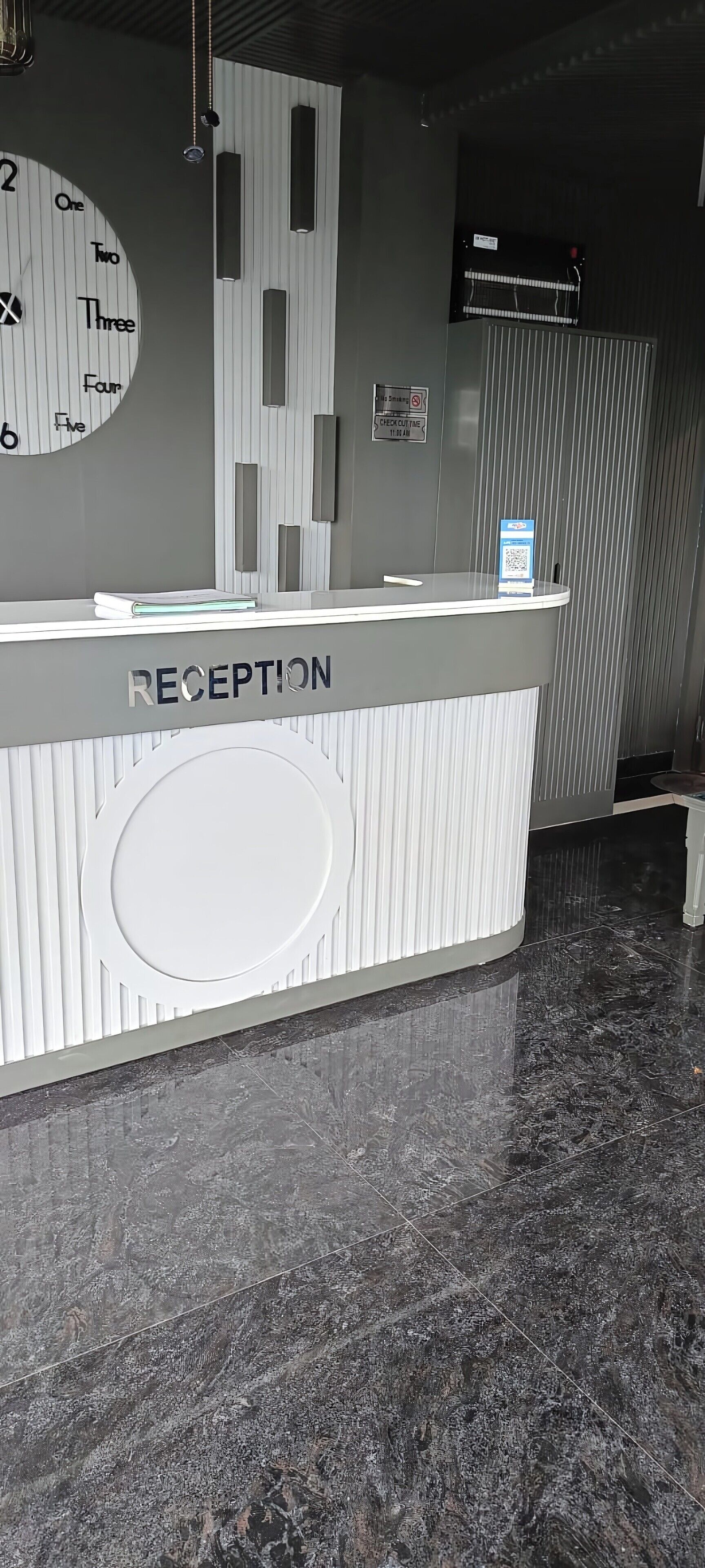 A reception desk with a clock, a sign indicating a smoking area, and a QR code for check-in.