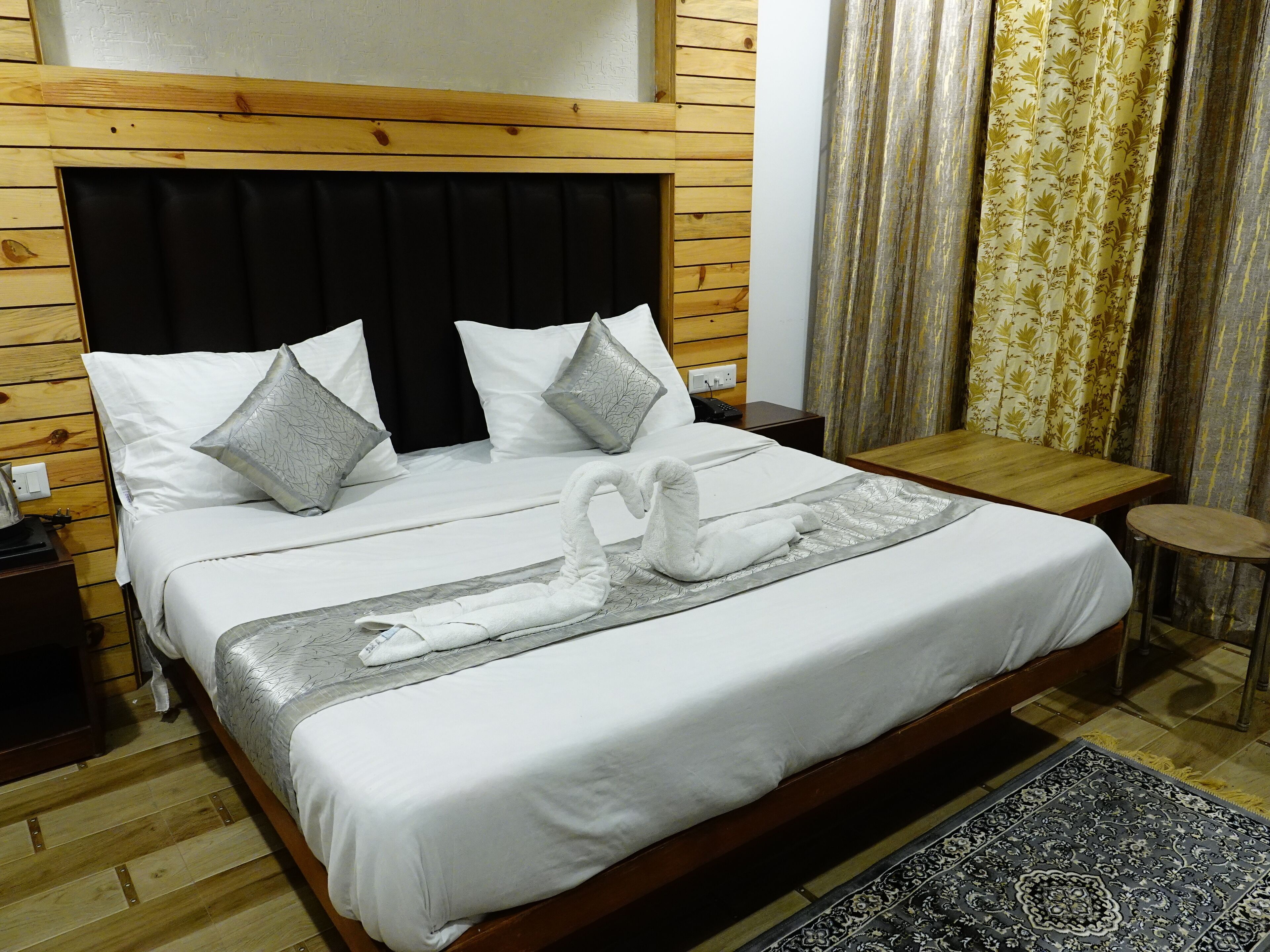 A neatly made bed with white linens, grey pillows, and a swan towel arrangement.